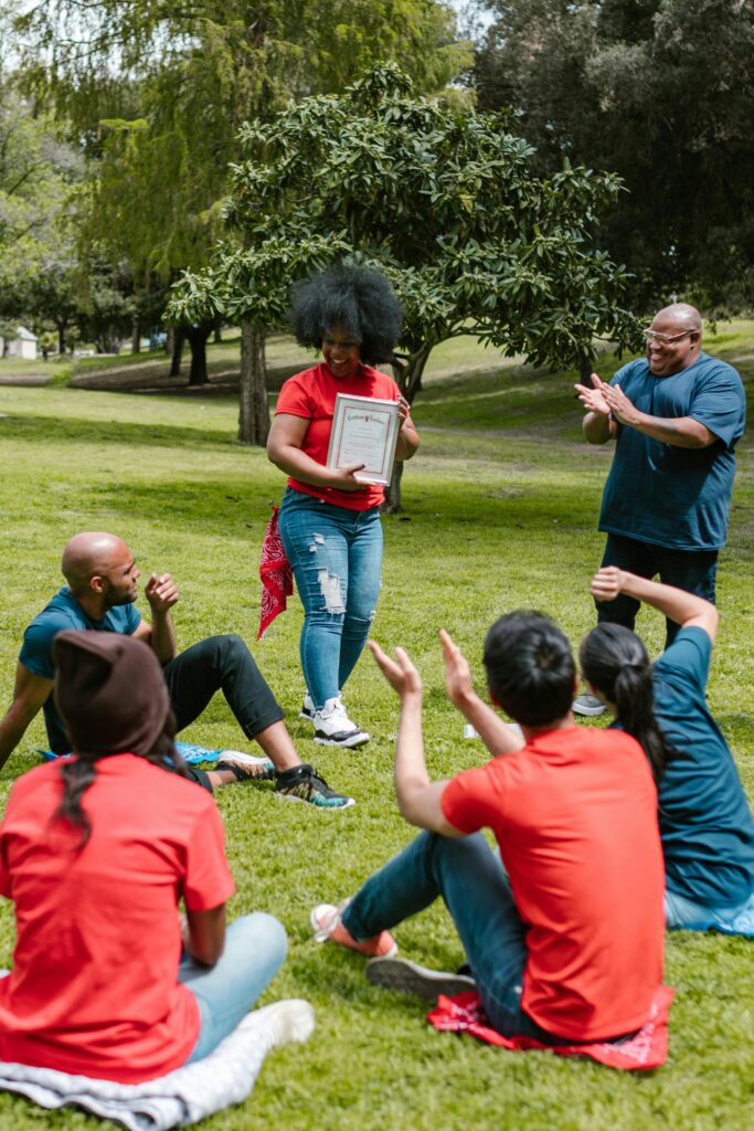 A group of adults celebrating an award outdoors in a park setting.